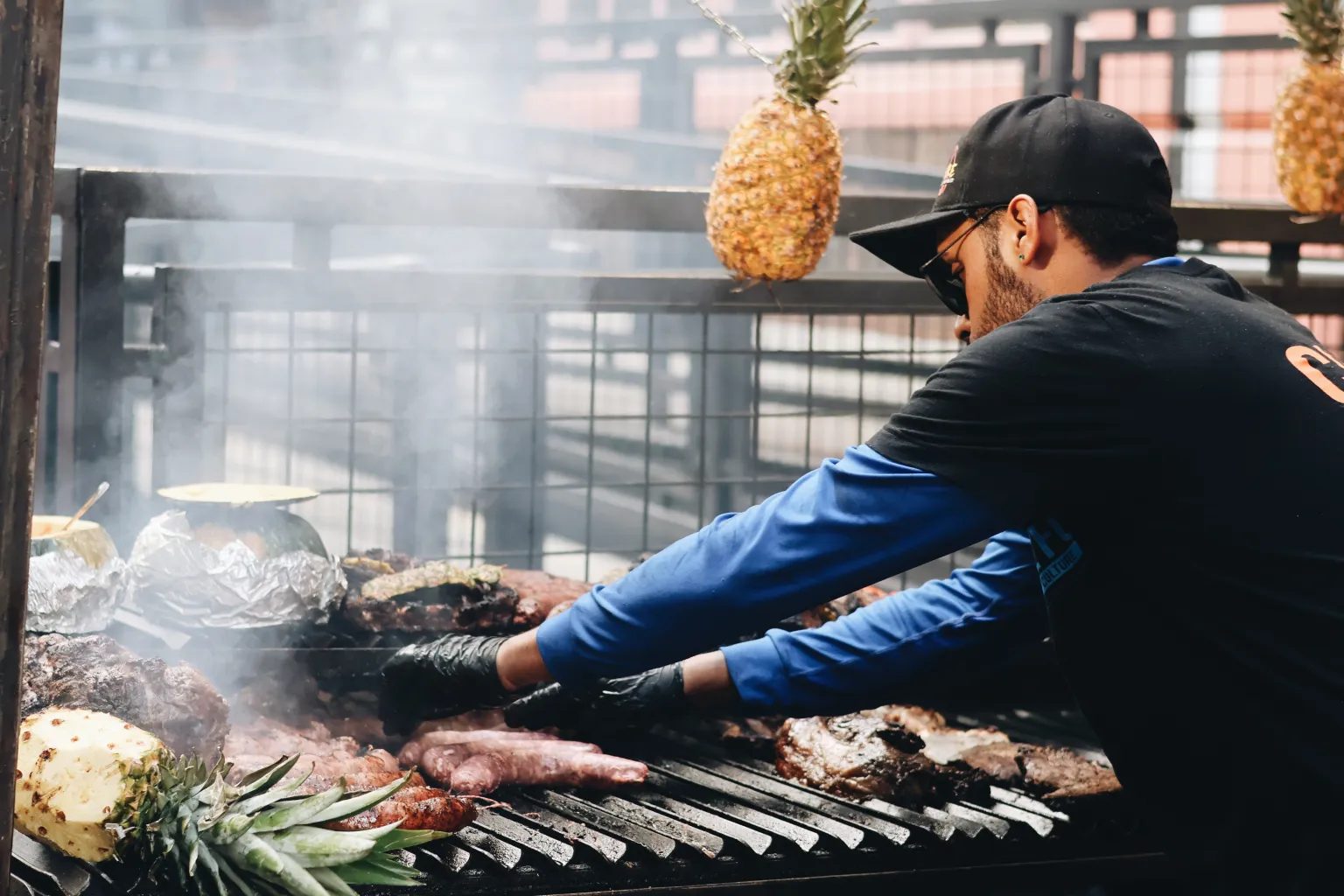 Vendor grilling meats with hanging pineapples